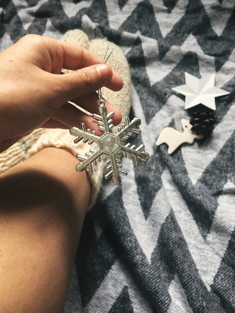 手握时尚的圣诞雪花在圣诞的背景羊毛袜腿上，节日装饰品在乡村毛毯。大气舒适的形象，暖冬的心情。手机照片图片下载