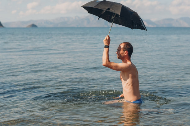 一个年轻人撑着伞在海里游泳。晒伤的概念。图片下载