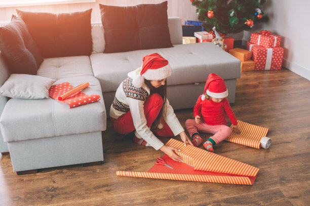 圣诞快乐，恭贺新禧。一张年轻女子和她女儿坐在地板上的照片。成人礼品包装盒。孩子回头看。她触动纸。图片下载