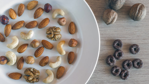 一个白色盘子里放杏仁，榛子，核桃，腰果，三个完整的核桃，松脆的全麦谷物，轻木桌上放圆形的燕麦。采购产品健康有机零食，早餐，食品配料。图片下载