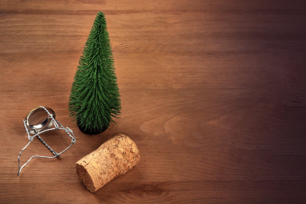 这是一张玩具圣诞树的照片，上面有香槟软木塞和封盖，背景是黑色的乡村木，带有复制空间，这是一个新年设计模板图片下载