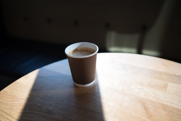 透过窗户的自然光照射在咖啡馆的木柚木桌子上的纸杯咖啡/早晨的时间/广告空间/独立的杯子/有背景的近距离物体/图片下载