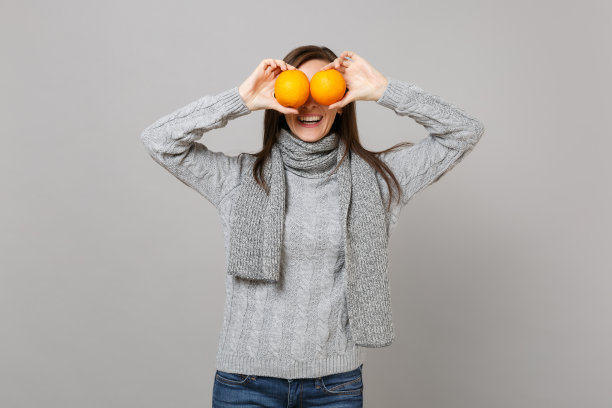微笑的年轻女子在灰色毛衣围巾覆盖眼睛与橙色孤立在灰色背景在工作室。健康时尚的生活方式，人们真诚的情感，寒冷的季节理念。模拟拷贝空间。图片下载