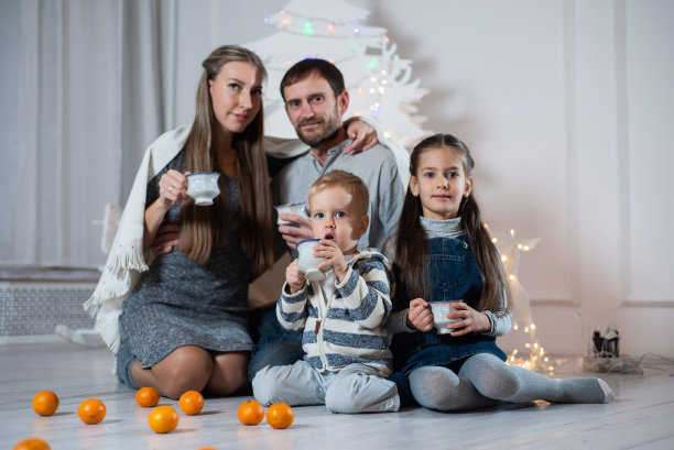 一个幸福家庭的圣诞照片。父亲，母亲，女儿和儿子坐在地板上喝茶，周围的橘子图片下载