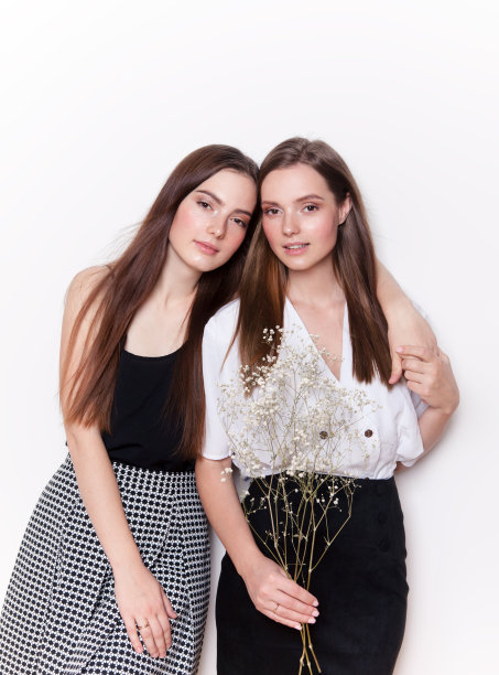 两个快乐可爱美丽的女人姐妹微笑着看美丽快乐的时装模特工作室肖像在白色的背景图片下载