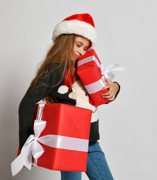 小女孩小孩戴着圣诞老人助手帽，带着红色的礼品盒开心地笑着喊图片下载