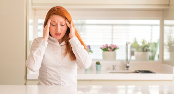 在厨房里的红发女人因为压力而手背疼痛。遭受偏头痛。图片下载