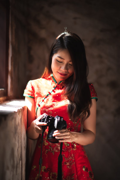 美丽的亚洲华人女性穿着红色旗袍，看着相机查看在中国新年旅行中拍摄的照片图片下载