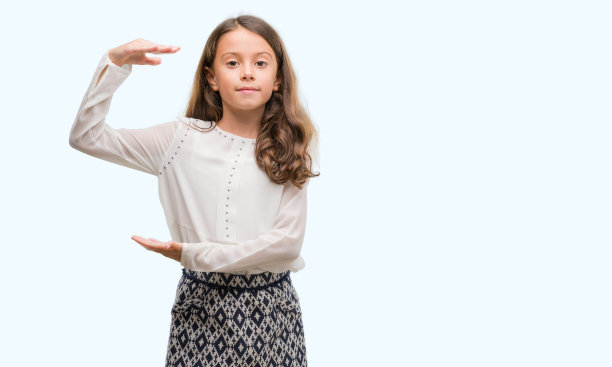 深色头发的西班牙裔女孩用手比划着大而大的尺寸符号，测量符号。看着镜头微笑。测量的概念。图片下载