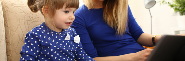 可爱的小女孩和妈妈在沙发上使用笔记本电脑图片下载