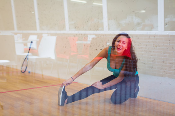在壁球场，一个可爱的年轻女子拿着球拍靠在墙上，图片下载