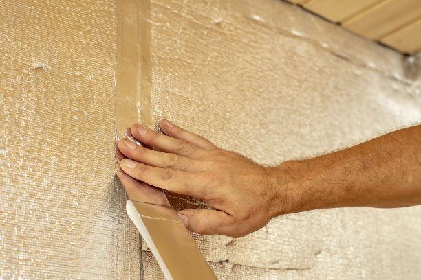 男手用铝胶带将接缝处的绝缘箔粘贴到墙面上。图片下载