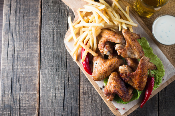 烧烤鸡翅与薯条和啤酒的特写照片。烤肉配酱汁，番茄酱，蛋黄酱。快餐和垃圾食品的概念。图片下载