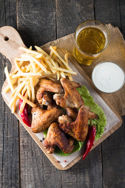 烧烤鸡翅与薯条和啤酒的特写照片。烤肉配酱汁，番茄酱，蛋黄酱。快餐和垃圾食品的概念。图片下载