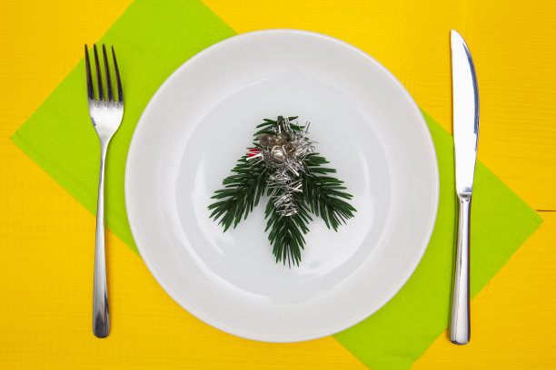 黄色的木桌上放着白色的盘子和绿色的圣诞装饰品图片下载