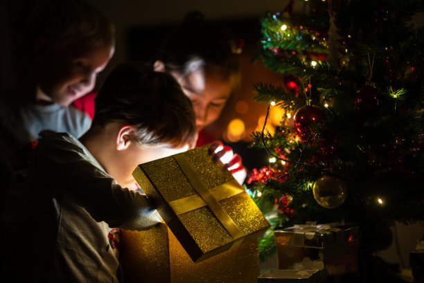 三个孩子，两个刚学走路的男孩和一个女孩，正在打开一个金色的礼盒图片下载