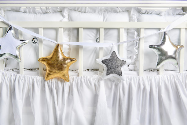白色婴儿床上放着银色、金色和白色的星形枕头图片下载