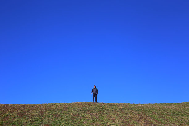 在美丽的、阳光明媚的秋日，一个成年的徒步旅行者站在草地上的地平线上图片下载
