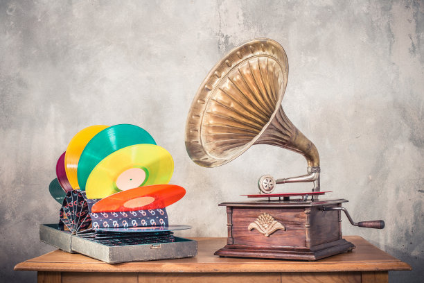 古董古董留声机唱机转盘与黄铜喇叭和彩色乙烯基唱片在老的特殊持有人手提箱木制桌子前混凝土墙背景。复古旧风格滤镜照片图片下载