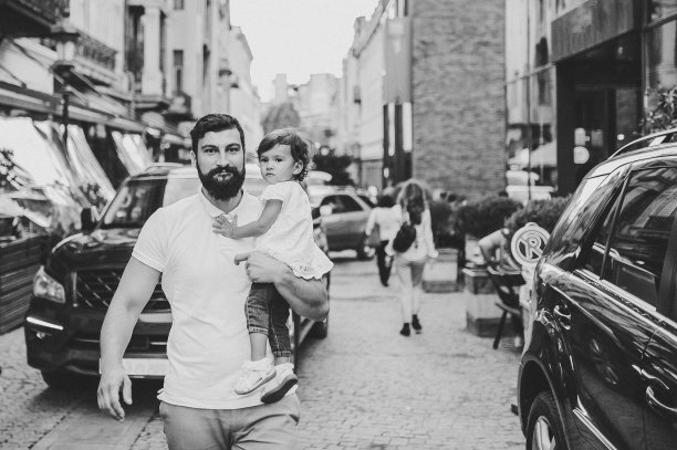 年轻幸福的家庭:父亲和女儿在城市的街道上散步，在户外。家庭度假和旅行的概念。爸爸抱着小女孩。黑白照片。图片下载