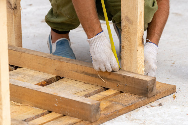 近距离裁剪的照片，不认识的工人在白色防护手套拿着测量在手靠近木板上的特殊建筑或柱模板图片下载