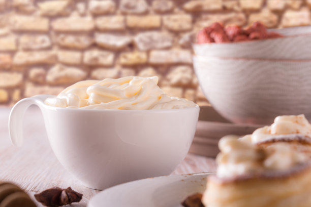 白色杯子的横向照片。杯子里装满了甜凝奶酪。杯子或碗放在破旧的白色和棕色木板上。八角香料周围都是球。图片下载