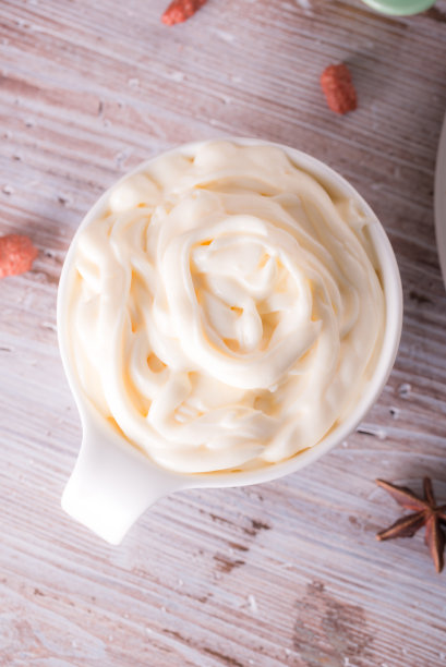 白色杯子的垂直照片。杯子里装满了甜凝奶酪。杯子或碗放在破旧的白色和棕色木板上。八角香料周围都是球。图片下载