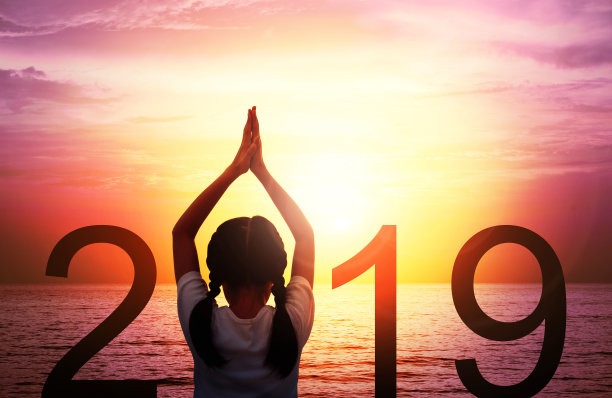 2019年新年贺卡。女孩的剪影做瑜伽vrikshasana树在热带海滩与美丽的日落天空的背景。孩子们站着看日出，这是2019号标志的一部分。素材图片