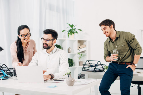 年轻的经理拿着一杯水看着办公室里的同事图片下载