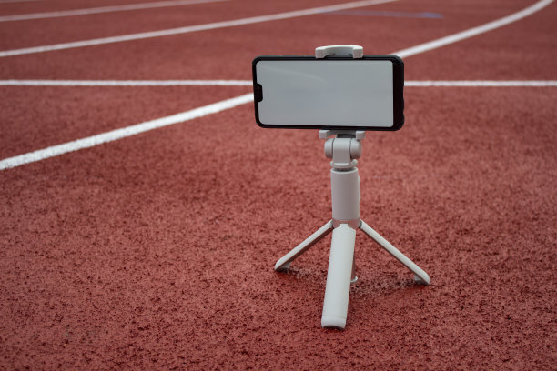 模拟的黑色智能手机和三脚架。白色屏幕为设计模板的背景红色跑道和体育场。图片下载