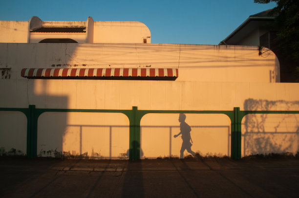 美丽的阴影女人跑在奶油墙的背景。夕阳照在墙和房子周围。运行孤立的剪影影子。浅蓝色的天空背景。温暖的基调。冬天的季节。图片下载