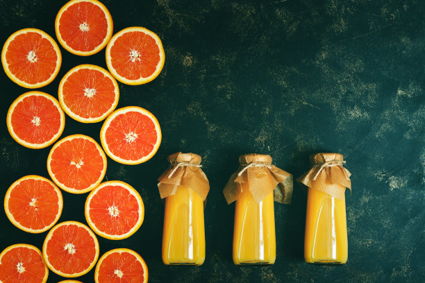 瓶子里的橙汁和深色背景上一半的橘色。俯视图，平放，复制空间。健康的维生素饮料。图片下载