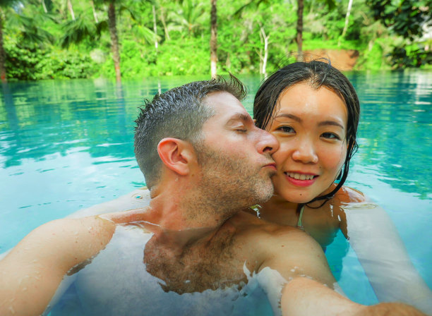 年轻快乐和美丽的混血亚洲女人和白人男人在热带度假胜地游泳池享受蜜月旅行庆祝爱情的浪漫自拍照片图片下载
