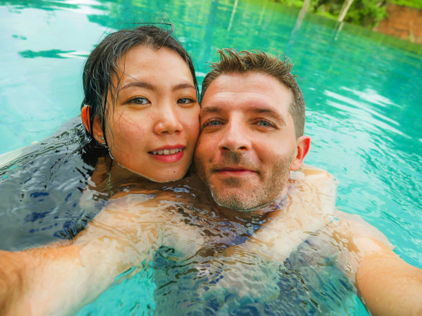 年轻快乐和美丽的混血亚洲女人和白人男人在热带度假胜地游泳池享受蜜月旅行庆祝爱情的浪漫自拍照片图片下载