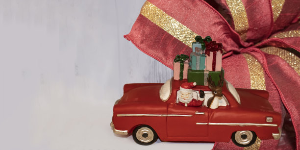 圣诞旗帜与玩具圣诞老人在复古汽车与驯鹿和一堆礼物在顶部，以一个明亮的背景与圣诞彩带-房间复制图片下载