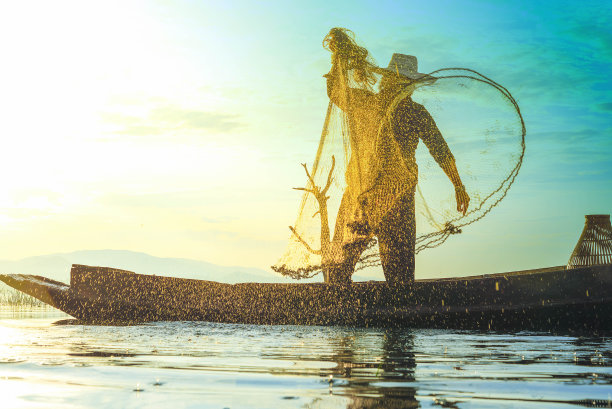 照片拍摄的水溅从渔民向湖上扔渔网。清晨的阳光下，渔夫拿着渔网的剪影。停止运动水滴。图片下载