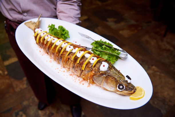 服务员手里的盘子里有加酱汁、柠檬和沙拉的烤鱼。图片下载