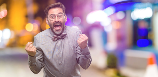 中年男子，留着胡子，打着领结，高兴而兴奋地庆祝胜利，表达巨大的成功，力量，能量和积极的情绪。庆祝新工作快乐图片下载