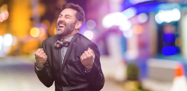 中年男子，留着胡子，打着领结，高兴而兴奋地庆祝胜利，表达巨大的成功，力量，能量和积极的情绪。庆祝新工作快乐图片下载