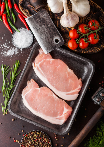 生的猪里脊排骨在塑料托盘里，配上盐和胡椒和老式的肉斧和铁锤在生锈的背景上。红辣椒，西红柿和大蒜。图片下载
