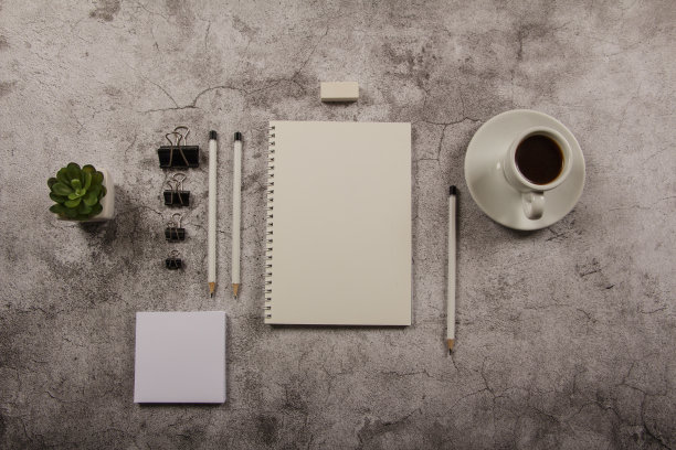 一个模版桌子的模型，一个空白信封，记事本和一杯咖啡和文具在一个灰色的背景。从以上观点。平的。为设计师设计布局。图片下载