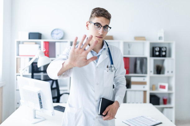 一个身穿白袍的年轻人站在办公室里，拿出一只手，手里拿着一个笔记本。图片下载