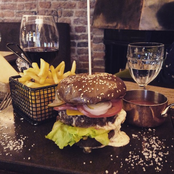 多汁的汉堡，肉，蔬菜和奶酪在一个餐馆的桌子上。在薯条旁边，一杯酒和一杯水。图片下载