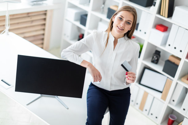 一个年轻的女孩坐在桌子上，手里拿着一张银行卡。图片下载