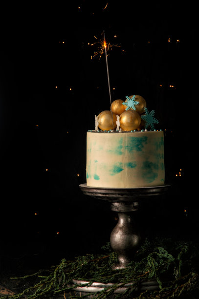 关闭了。圣诞蛋糕和一个燃烧的烟火来装饰它。黑色背景与圣诞灯。图片下载