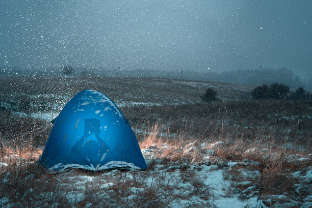 一个躺在帐篷里看书的男人的剪影。外面下雪了。图片下载