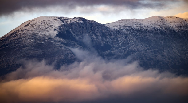 美丽的景色，一些雪山周围的软云在日落。图片下载
