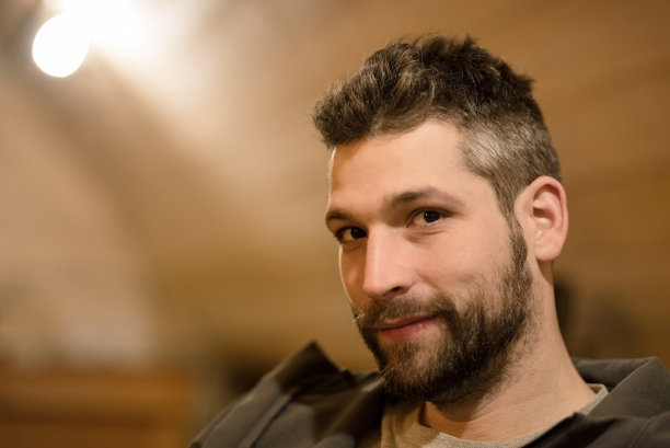 近距离的肖像英俊的年轻胡子男子坐在一个小木屋看着相机图片下载