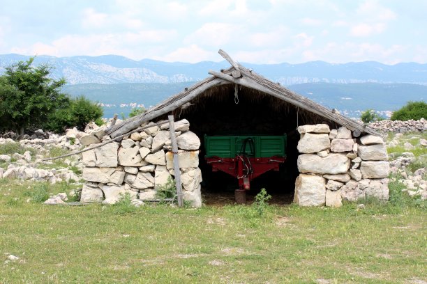 传统的地中海储存石头建筑，有干干草屋顶和停放在里面的拖拉机拖车图片下载