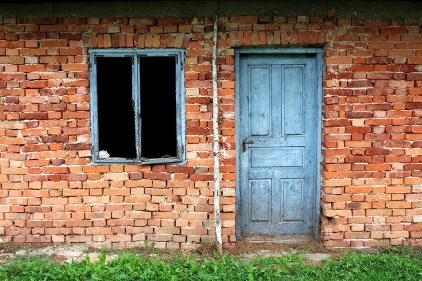 红色砖墙上挂着褪色的蓝色木门，旁边是破旧的无玻璃窗框图片下载